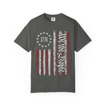 The We The People Distressed Flag Tee is a charcoal gray Comfort Colors 1717 unisex shirt featuring a distressed American flag, red and white stripes, a 1776 stars circle, and 1776-Stay Free in bold white script.