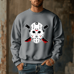 A man wears the Voorhees 13 Iconic Horror Sweatshirt, featuring a hockey mask and bloody knives. The blurred rustic background enhances the eerie vibe, perfect for horror enthusiasts.