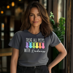 Indoors, a smiling woman wears the Treat All Peeps with Kindness! Easter tee adorned with colorful bunny silhouettes. Greenery and blurred lights behind her create a warm ambiance.