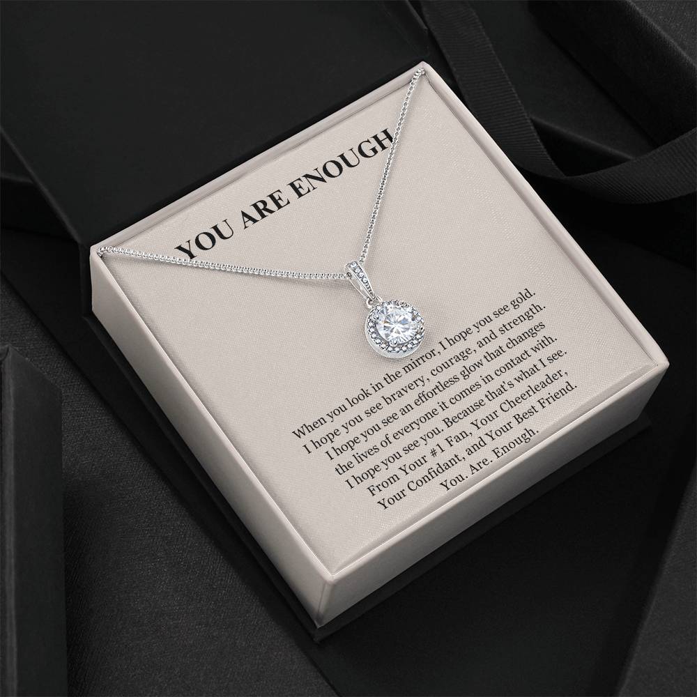 The Eternal Hope Necklace - You Are Enough comes in a black box with a silver round pendant and a card that reads YOU ARE ENOUGH, inspiring inner strength and self-love. A light interior adds an elegant touch.