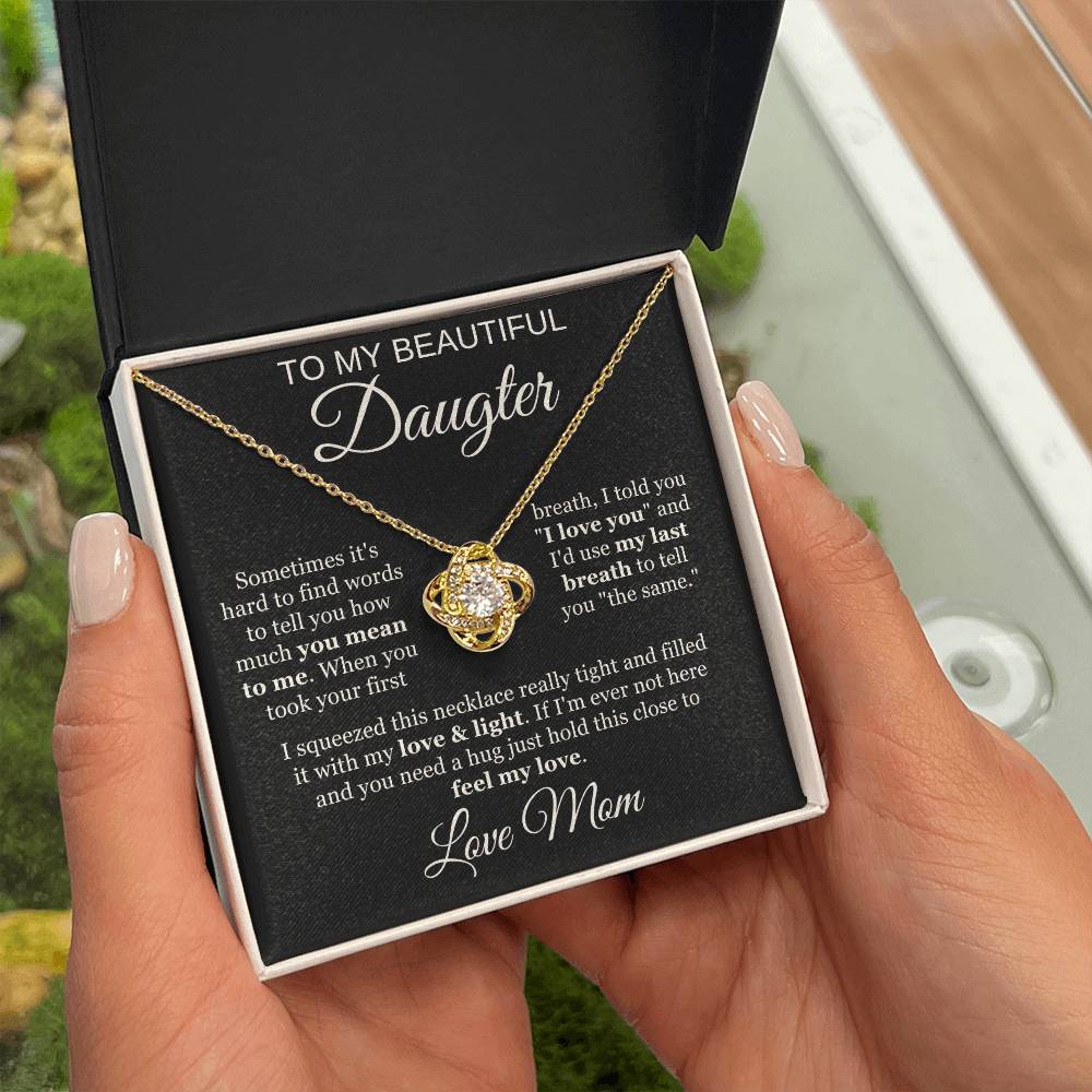 A person holds an open box with a 14k white gold To My Beautiful Daughter Cubic Zirconia Love Knot Necklace and a heartfelt message card for their daughter from mom, set against a black background—perfect for graduation or birthday gifts.