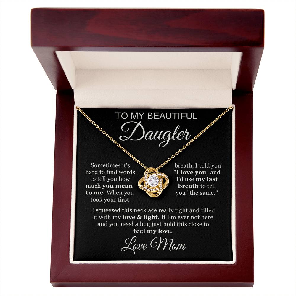 The To My Beautiful Daughter Cubic Zirconia Love Knot Necklace features a heart-shaped pendant with sparkling crystals, presented in an open wooden box with a black message card expressing a mothers love. Perfect for graduation or birthday gifts.