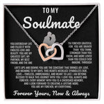 Elegant two-tone interlocking heart necklace displayed in a wooden gift box with a heartfelt soulmate message, set against a backdrop of soft glowing lights.