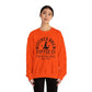 Wearing the Witches Brew Coffee Co. Sweatshirt - Stop in for a Spell! in vibrant orange, adorned with a witch hat design and dark hair pulled back, a person stands against a plain white background, showcasing the ultimate Halloween style.