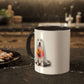 The Ghostly Pup Halloween Mug – Spooktacular Coffee Companion features a cute dog in a ghost costume with a pumpkin basket. Set on a kitchen counter next to nuts on a plate, its charming design stands out against the softly blurred background.