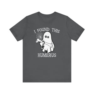 The I Found This Humerus - Funny Halloween Ghost T-Shirt is a dark gray tee with a playful ghost holding a bone and spider web, plus white lettering saying I FOUND THIS HUMERUS for extra spooky fun.