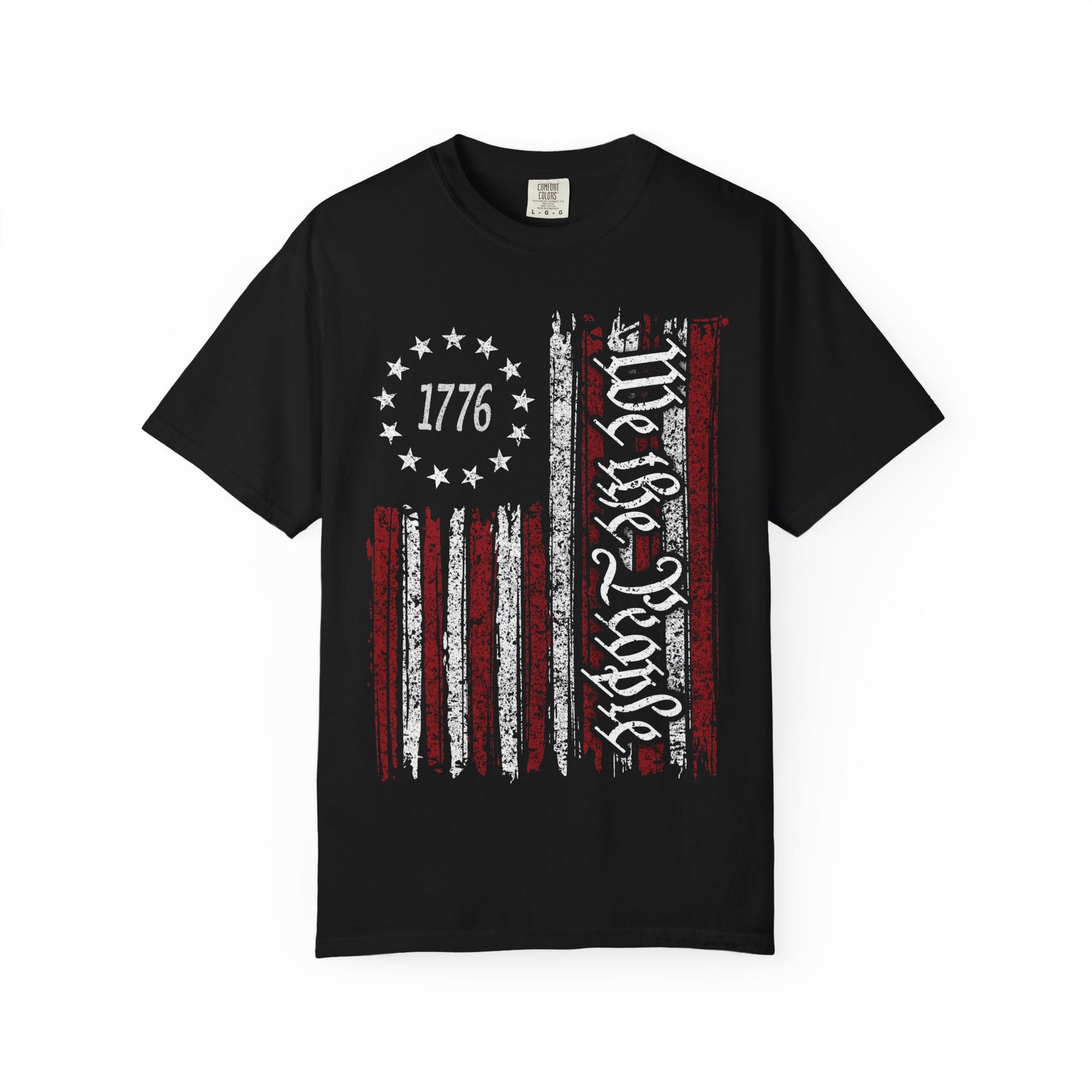The We The People Distressed Flag Tee (Comfort Colors 1717) features a black unisex design with a vintage American flag, vertical “We the People” in white, and “1776” surrounded by thirteen stars— ideal patriotic apparel for history enthusiasts.