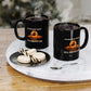Two steaming black mugs with On a Dark Desert Highway designs exude spooky charm on a round tray with a spoon. Nearby, two macarons sit on a small plate, perfect for coffee lovers. The background is blurred for effect.