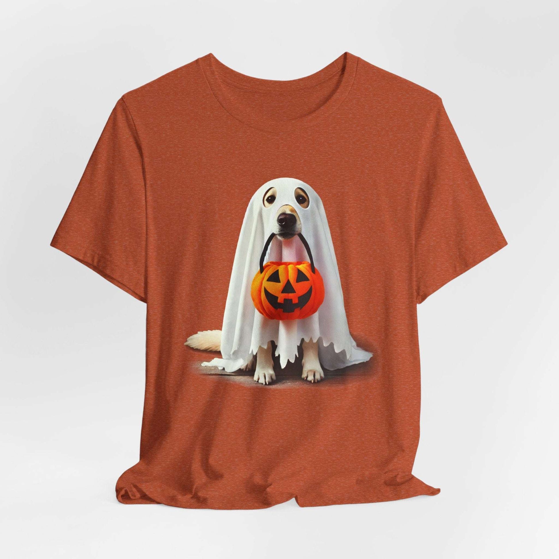 The Ghostly Pup Halloween T-Shirt features a cute dog dressed as a ghost with a sheet over its head and holding a pumpkin-shaped trick-or-treat bucket. This adorable design comes on a unisex jersey short sleeve tee.