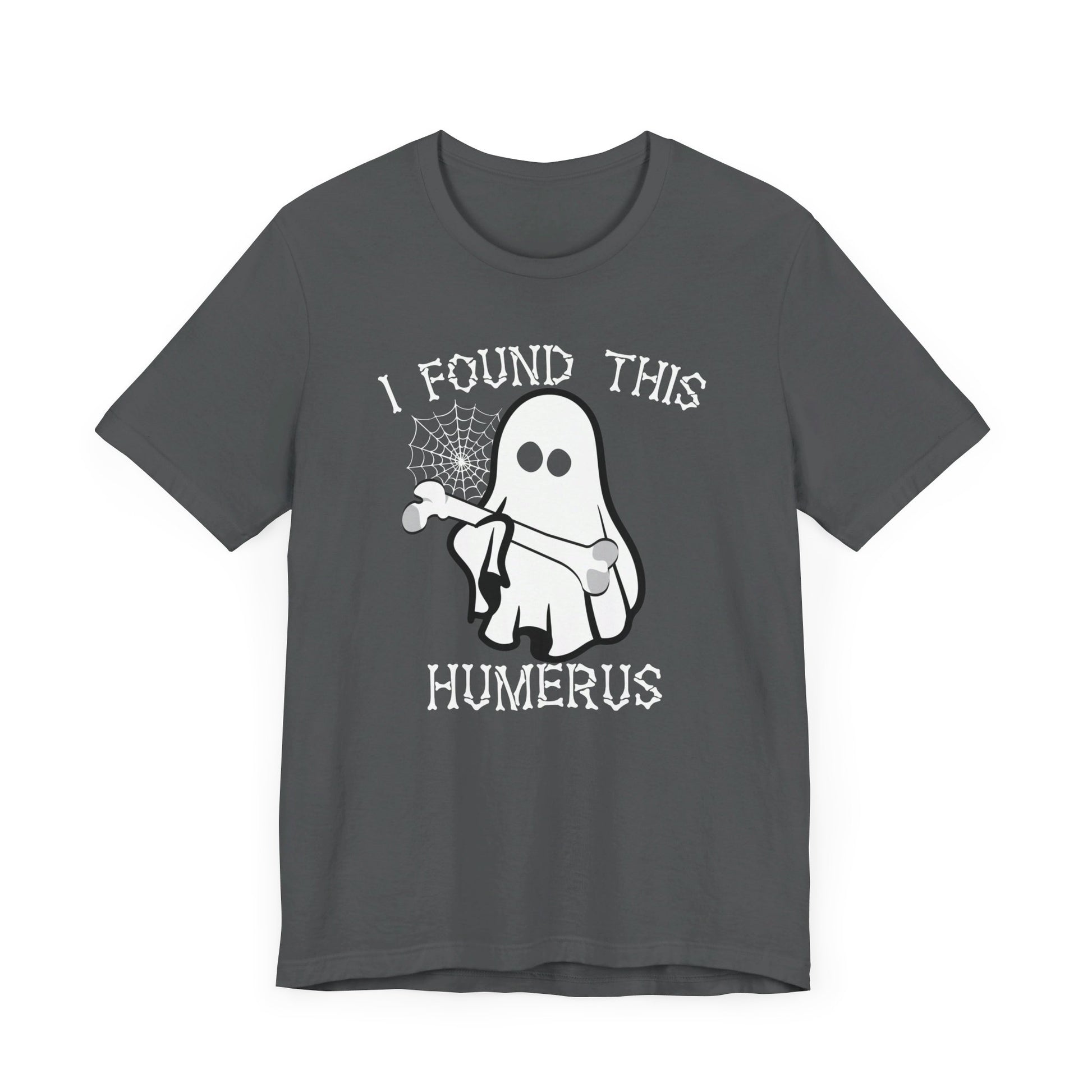 The I Found This Humerus - Funny Halloween Ghost T-Shirt is dark gray, featuring a ghost holding a bone by a spider web. White text above and below reads: I FOUND THIS HUMERUS, giving it humorous and spooky Halloween vibes.