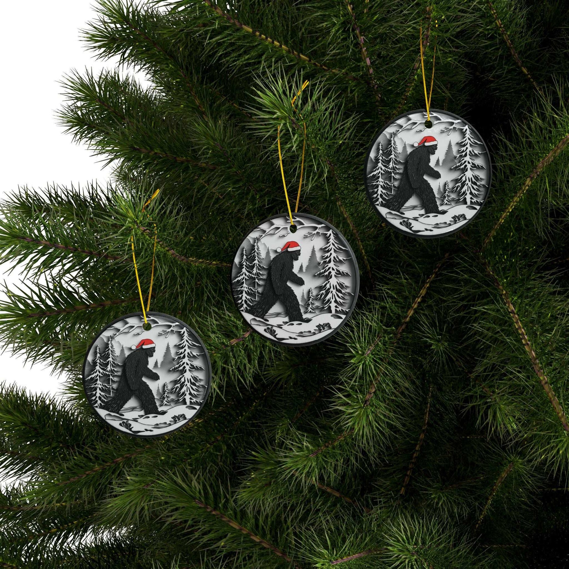 Round Christmas ornament featuring a black Bigfoot silhouette wearing a Santa hat, walking through a snowy forest scene.