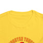 Close-up of the top part of a yellow Monster Truck Rex T-Shirt 🛻🦕 – Toddler Boys Tee, with orange and red text partially visible near the bottom edge. The shirt is laid flat on a white background.