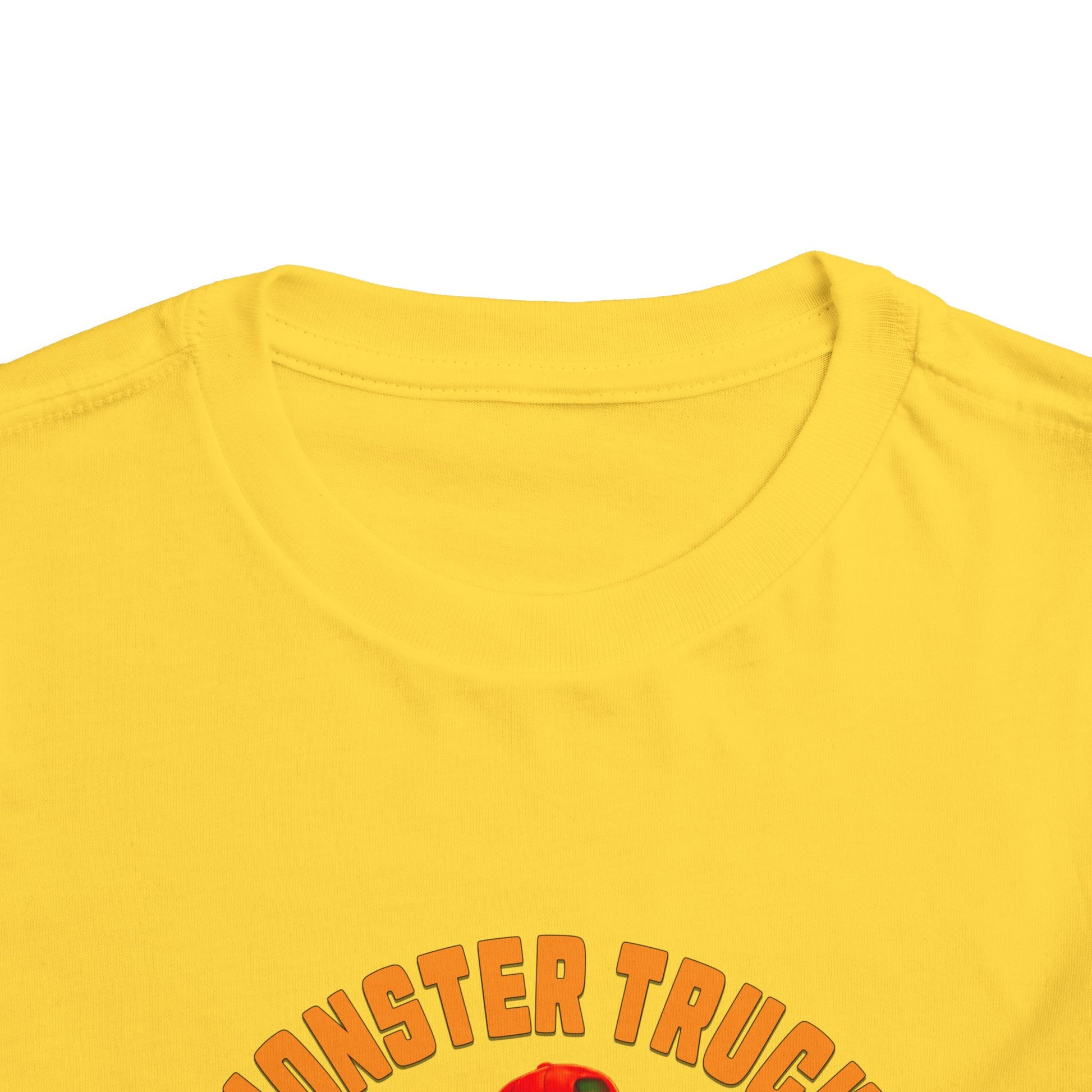 Close-up of the top part of a yellow Monster Truck Rex T-Shirt 🛻🦕 – Toddler Boys Tee, with orange and red text partially visible near the bottom edge. The shirt is laid flat on a white background.