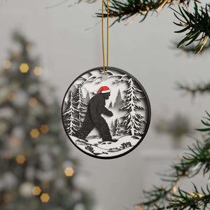 Round Christmas ornament featuring a black Bigfoot silhouette wearing a Santa hat, walking through a snowy forest scene.