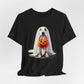 The Ghostly Pup Halloween T-Shirt features a cute ghost dog in a white sheet with eye holes, holding an orange jack-o-lantern bucket, perfect for unisex spooky style.