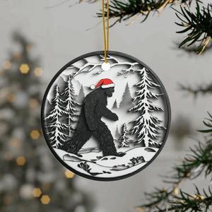 Round Christmas ornament featuring a black Bigfoot silhouette wearing a Santa hat, walking through a snowy forest scene.