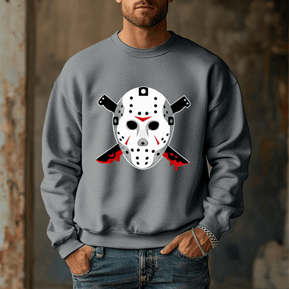 A man wears the Voorhees 13 Iconic Horror Sweatshirt, featuring a hockey mask and bloody knives. The blurred rustic background enhances the eerie vibe, perfect for horror enthusiasts.