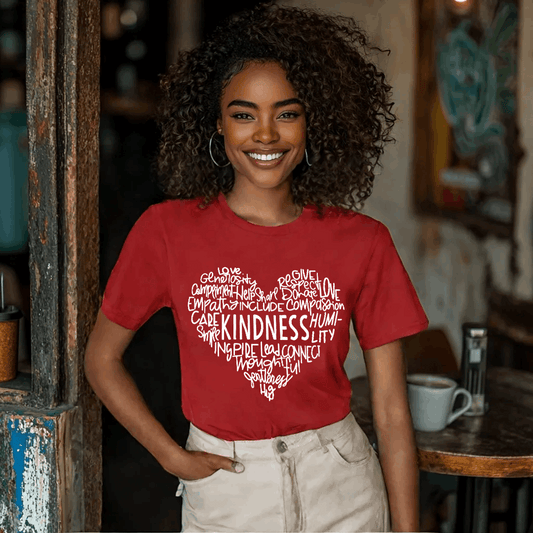 Woman wearing a red t-shirt featuring a heart-shaped word art design with kindness-related words in white text.