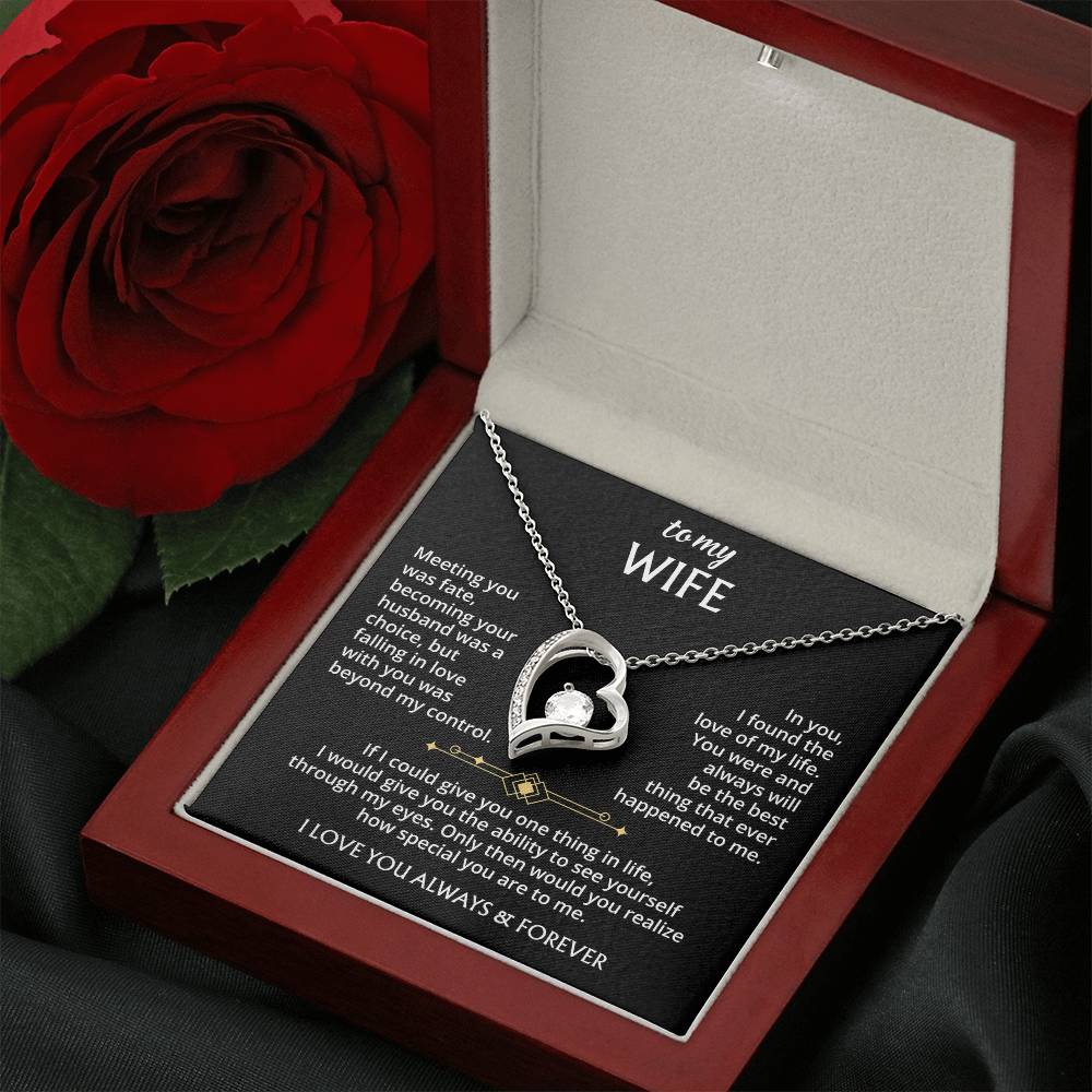The To My Wife – Forever Love Necklace, a silver heart-shaped pendant with a sparkling crystal, rests in an open red jewelry box with a message of fate and devotion, beside a red rose on black fabric.