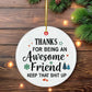 Round white Christmas ornament with a humorous appreciation message for an awesome friend, decorated with festive icons and hung on a holiday tree.