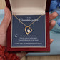 A hand holds an open wooden box with a Forever Love Necklace inside, featuring a heart-shaped pendant in white gold finish. The message reads: To my granddaughter, no matter the distance, you will always be in my heart. I love you to the moon and back.
