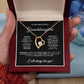 A hand opens a red box to reveal the Forever Love Necklace featuring a heart-shaped pendant with a cubic zirconia gem and gold finish. The lid displays a heartfelt message for a granddaughter against black, with a blue flower visible. Product: To My Beautiful Granddaughter - Forever Love Necklace with Heartfelt Message Card.