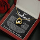 Gold heart pendant necklace with a sparkling crystal, displayed in a wooden gift box with a romantic message for a soulmate, surrounded by rose petals.