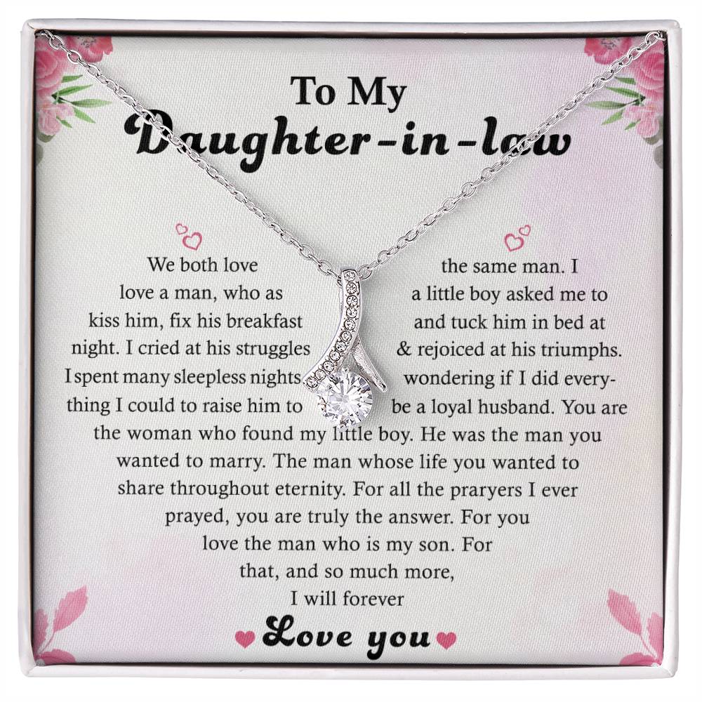 The To My Daughter-in-Law - Alluring Beauty Necklace features a silver, ribbon-shaped pendant in a 14k white gold finish on a card with a heartfelt message and pink floral designs, expressing love and gratitude.