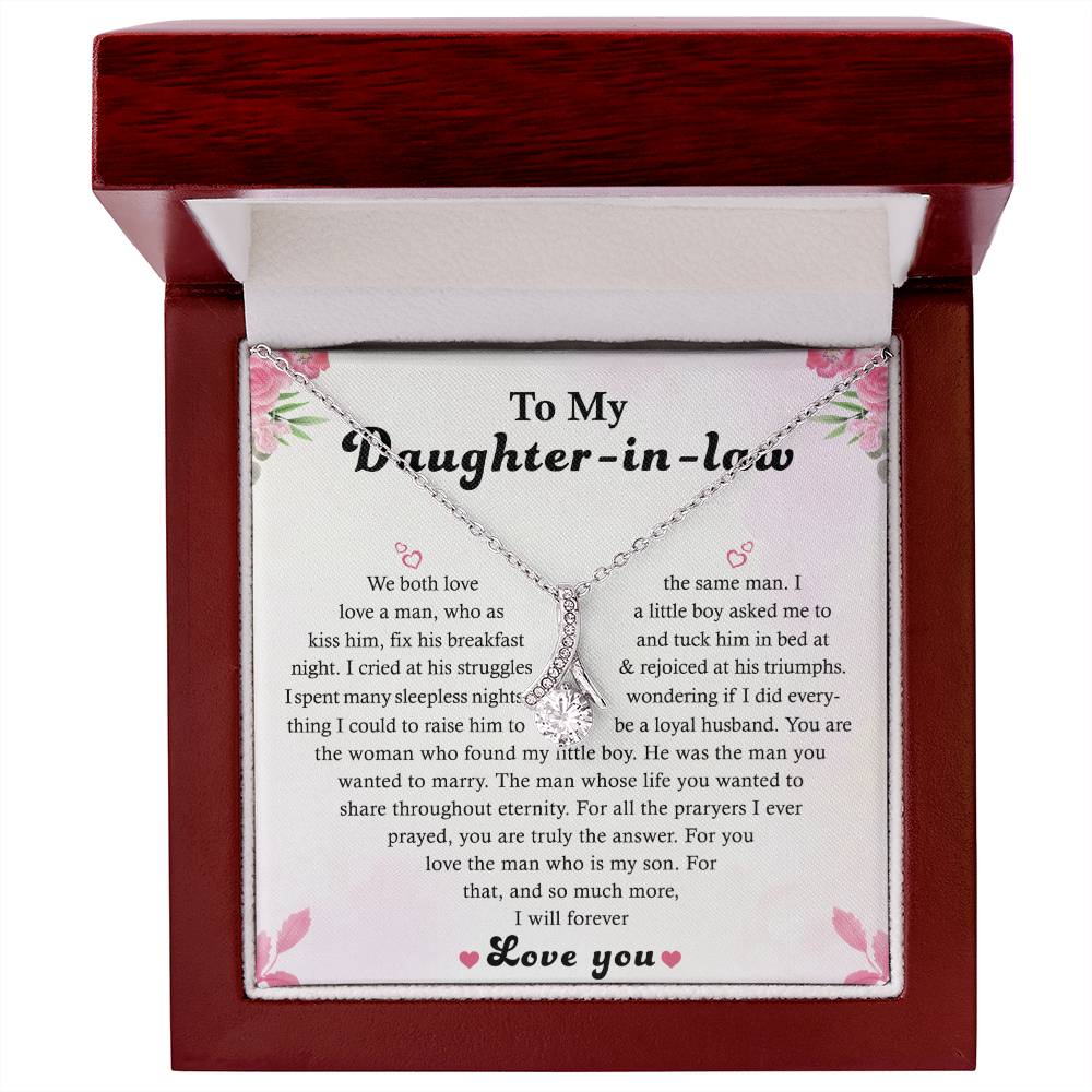 The To My Daughter-in-Law - Alluring Beauty necklace, ribbon-shaped and finished in 14k white gold, is beautifully presented in an open jewelry box. The lid contains a message expressing love and appreciation. The box features a wooden exterior with a white and pink interior.
