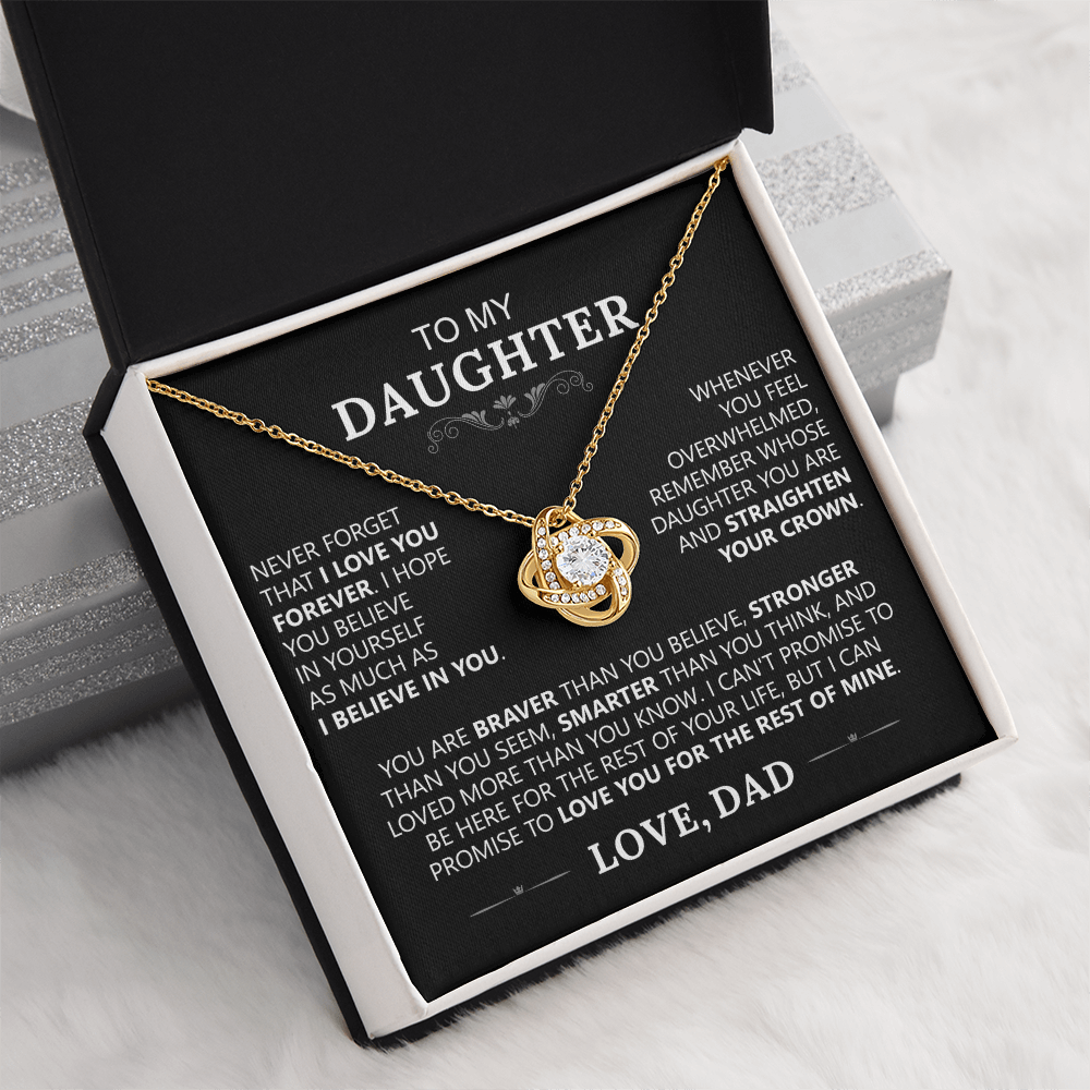 The To My Daughter - Love Knot Necklace features a gold knot pendant in a black box. Inside the lid is a heartfelt message from a father to his daughter about love, support, and encouragement, ending with “LOVE, DAD.”.