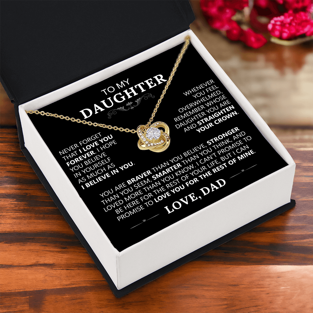 The To My Daughter - Love Knot Necklace sits in an open black gift box with a heartfelt printed message from father to daughter, expressing love and support. Red flowers appear in the background—an ideal gift for daughters.