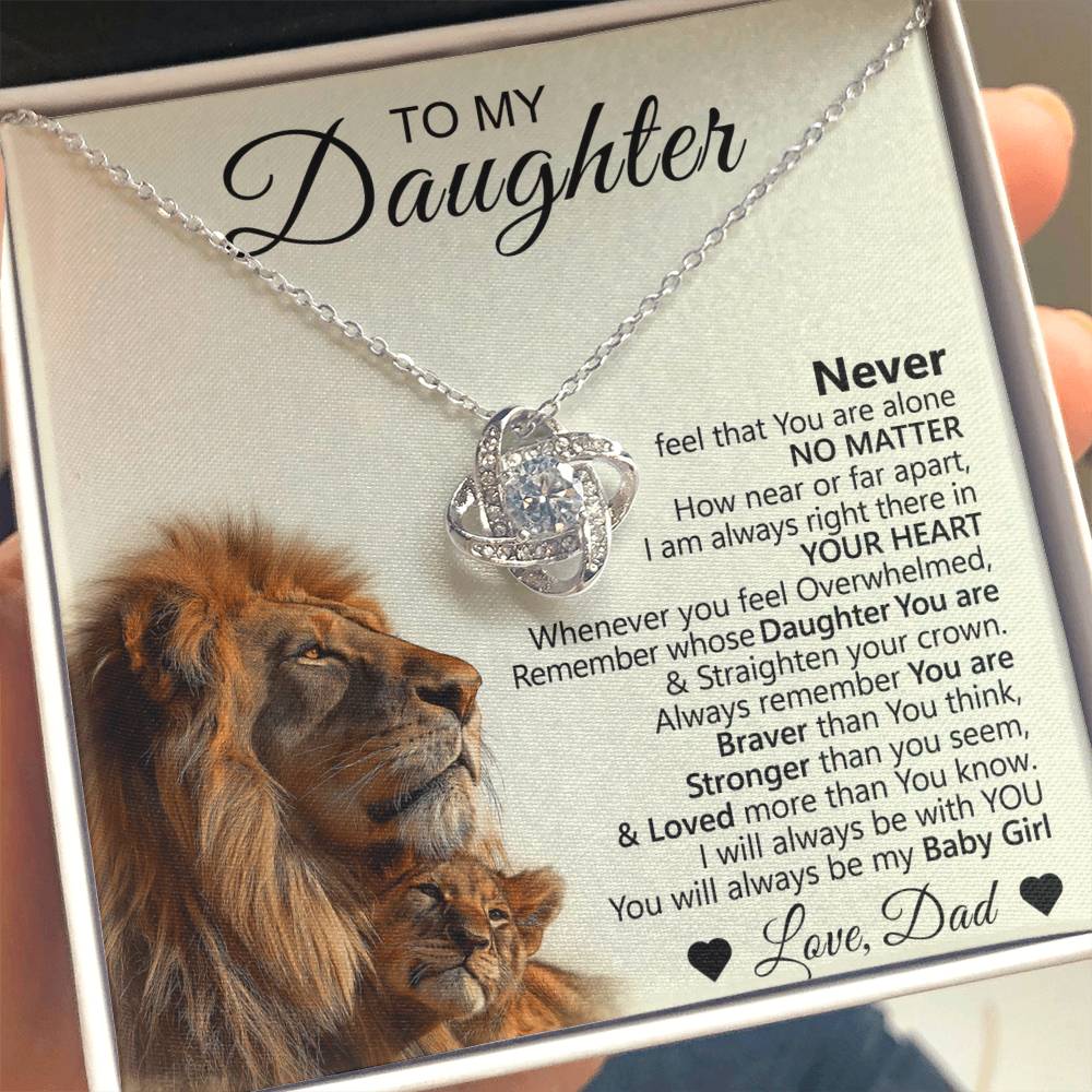 A person holds the To My Daughter – Love Knot Necklace with Lion & Cub Message Card, featuring a sparkling pendant in a box with a lion and cub illustration—a perfect gift symbolizing love, strength, and support from father to daughter.
