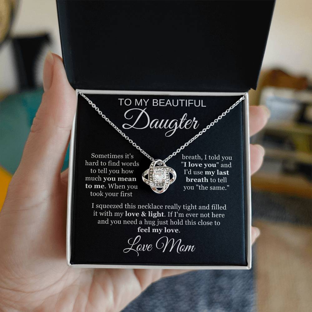 A hand holds an open jewelry box displaying the To My Beautiful Daughter Cubic Zirconia Love Knot Necklace on a black message card background—a sparkling 14k white gold necklace with a heartfelt note from mother to daughter.