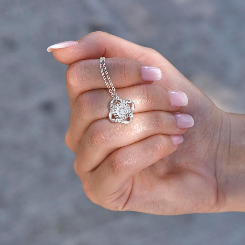 A manicured hand holds a delicate silver Love Knot Necklace with a sparkling round pendant—an ideal gift, presented on a “To My Daughter” Lion & Cub message card.