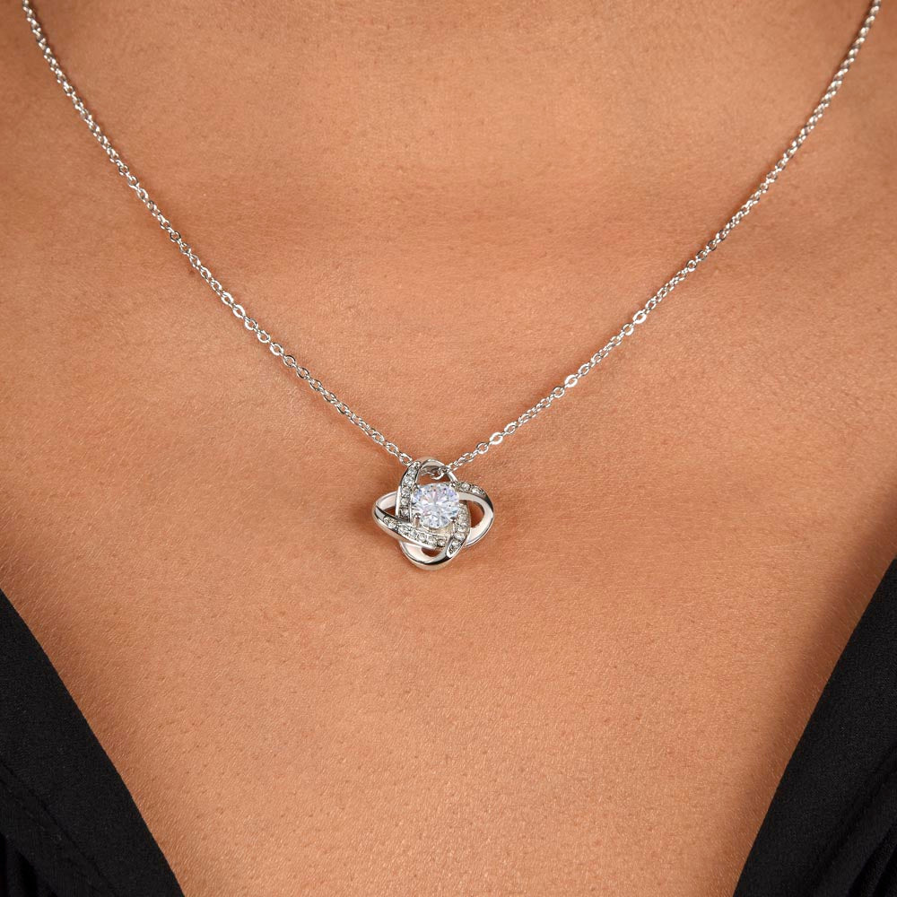 A close-up of a person wearing the To My Daughter – Love Knot Necklace with a sparkling pendant, set against bare skin and a black V-neck top, shown with the Lion & Cub Message Card.