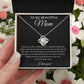 A hand holds an open gift box with the To My Beautiful Mom Cubic Zirconia Love Knot Necklace, featuring a sparkling pendant on a delicate chain and a heartfelt black message card for Mom—perfect for Mother’s Day or birthdays. Pink and white flowers surround the scene.
