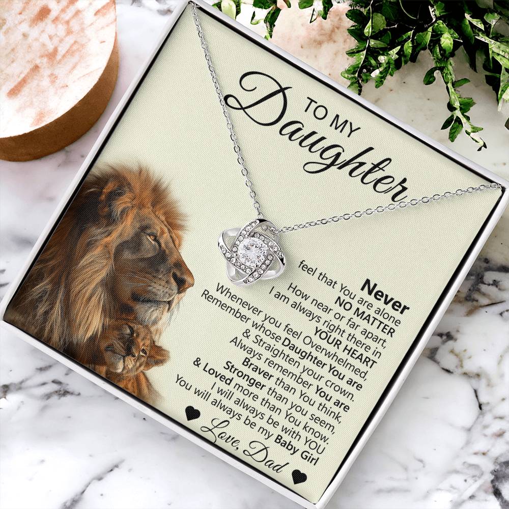 The To My Daughter – Love Knot Necklace with Lion & Cub Message Card features a silver intertwined heart pendant, presented in a box with a heartfelt father-to-daughter message, lion illustration, greenery, and a round wooden accent.