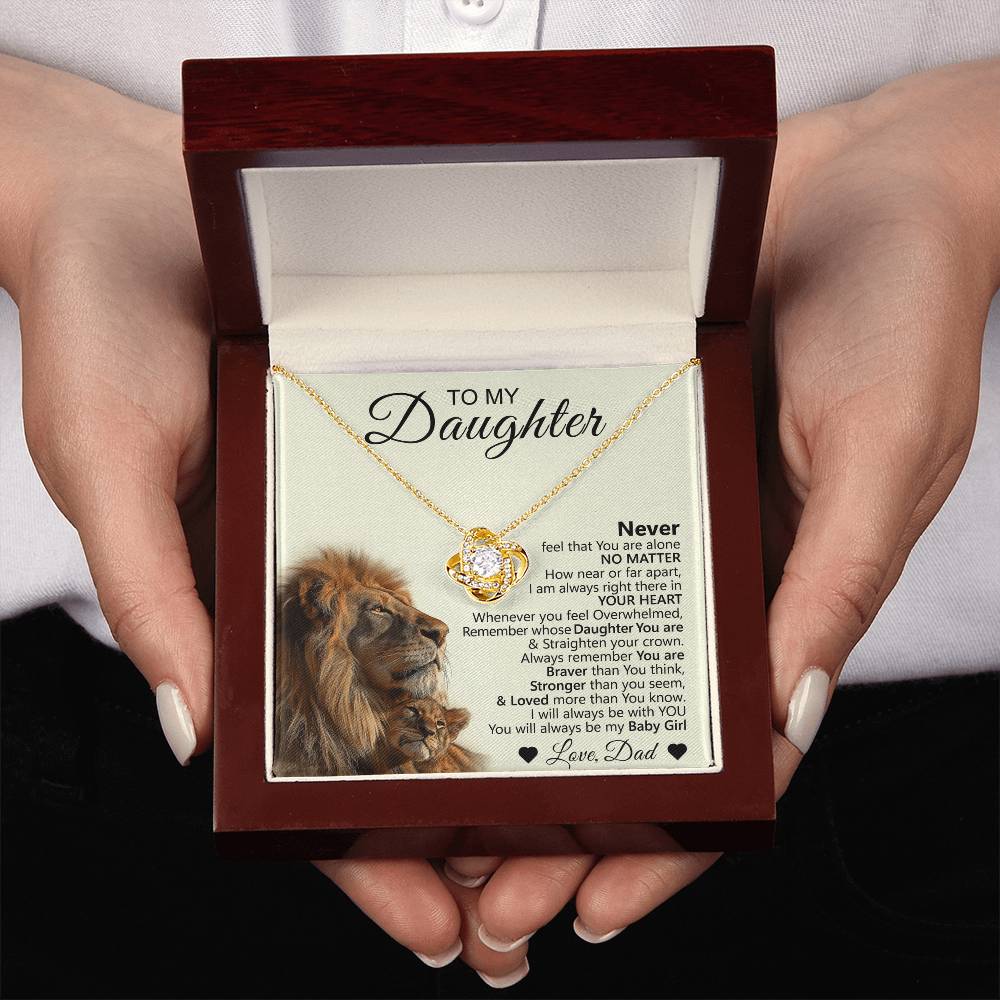 A person holds an open box with the To My Daughter – Love Knot Necklace and a card featuring a lion and cub—an ideal gift expressing love from dad to daughter.