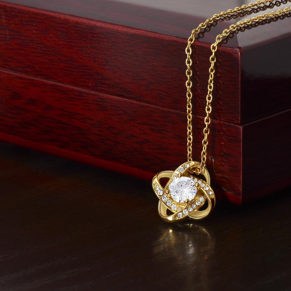 The To My Daughter – Love Knot Necklace features a sparkling central stone encircled by gold loops, beautifully presented on a dark jewelry box with a Lion & Cub message card—an ideal gift for your daughter.
