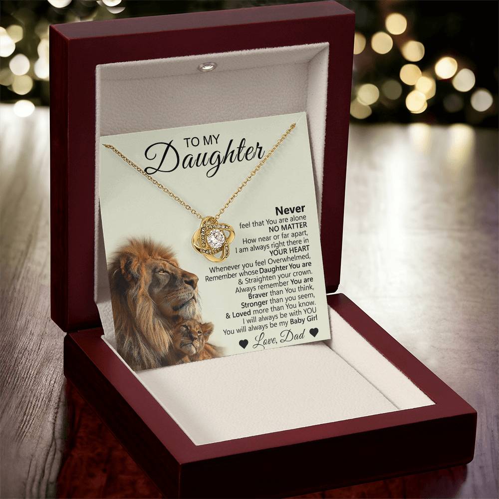 The To My Daughter – Love Knot Necklace with Lion & Cub Message Card comes in a red jewelry box and features an inspiring note from dad—a heartfelt gift for a daughter, beautifully presented with glowing blurred lights in the background.