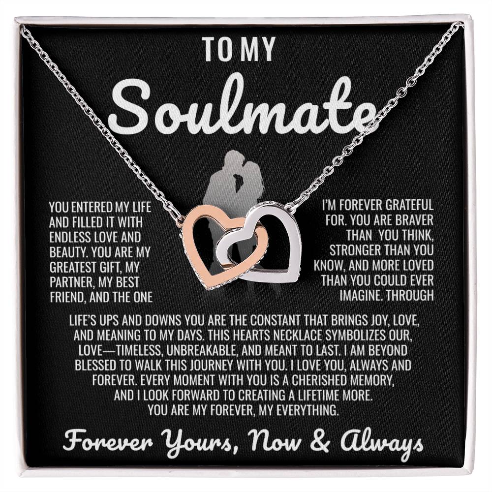 Elegant two-tone interlocking heart necklace displayed in a wooden gift box with a heartfelt soulmate message, set against a backdrop of soft glowing lights.
