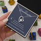A hand presents the To My Granddaughter - Forever Love Necklace with Heartfelt Message Card, featuring a heart-shaped pendant centered with a CZ crystal. The box lids message enhances this white gold finish treasure, while colorful gift boxes in the background add charm.