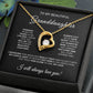The To My Beautiful Granddaughter - Forever Love Necklace with Heartfelt Message Card features a gold-finished heart-shaped pendant with a central cubic zirconia crystal, presented in a box with an affectionate message and surrounded by blue flowers for added elegance.